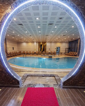 Ein großer Innenpool mit einem runden Rundgang, umgeben von Liegestühlen und einem roten Teppich, der zum Pool führt.