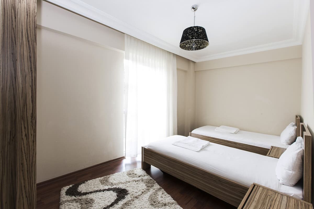 Une chambre d’hôtel avec deux lits, un plancher en bois, une grande fenêtre avec des rideaux et un luminaire suspendu.