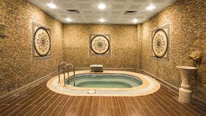 Ein Wellnessbereich mit einem runden Whirlpool, gefliestem Boden und dekorativen Wandverkleidungen.