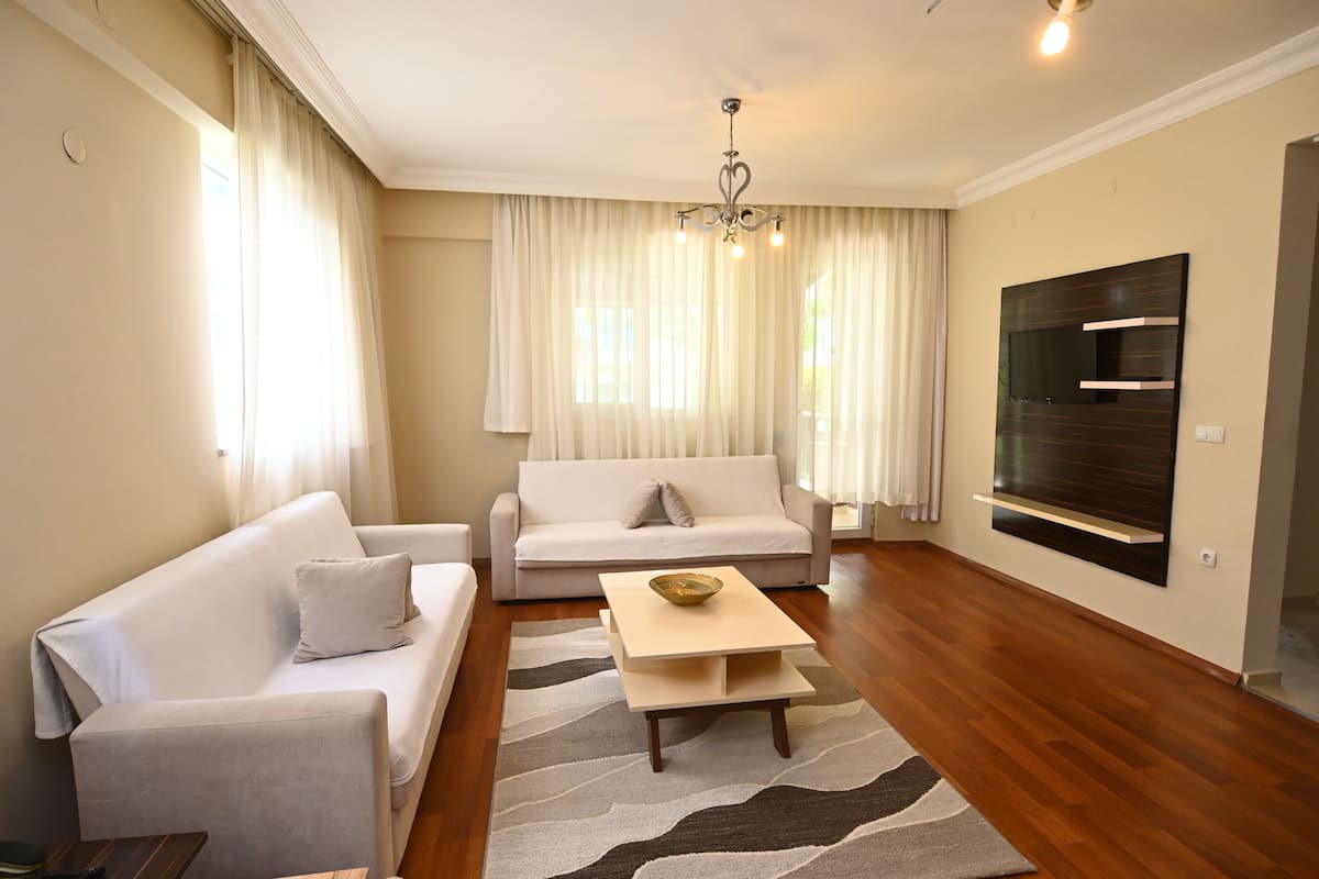 Un salon moderne avec deux canapés blancs, une table basse en bois et un grand téléviseur à écran plat fixé au mur.