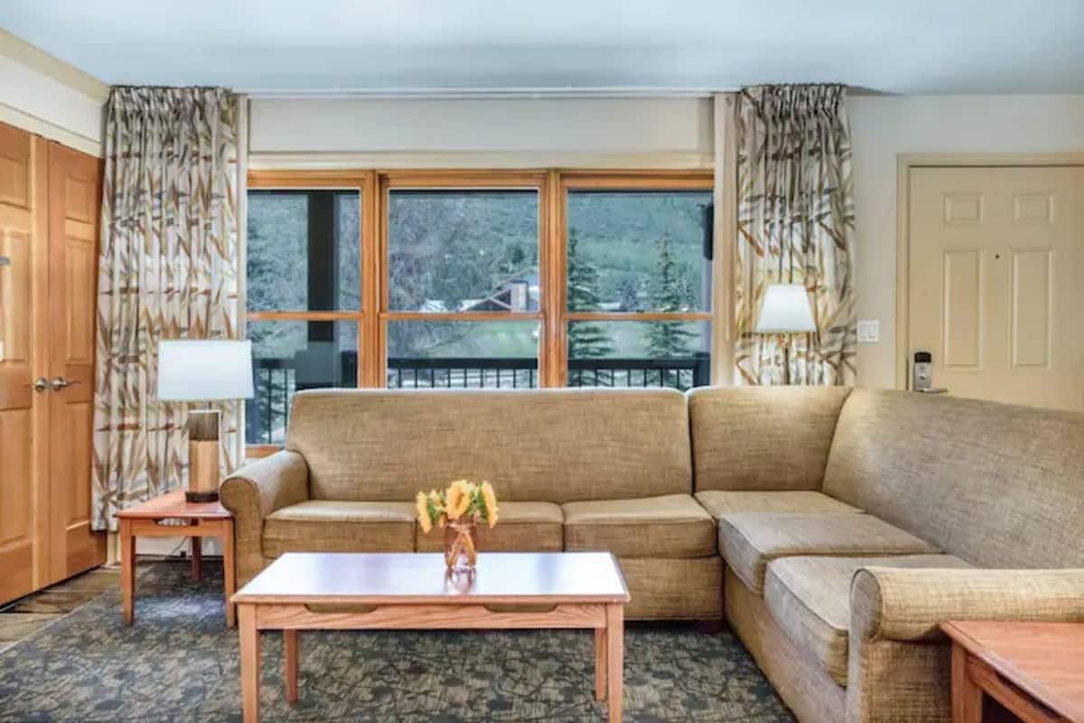A living room with a beige sofa, a wooden coffee table, and a window with curtains.