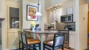 A kitchen with a central island, two bar stools, a microwave, and a coffee maker. - Aspen at Streamside at Vail (Vail)