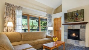 A living room with a sofa, a coffee table with flowers, a fireplace, and a painting of a mountain biker. - Aspen at Streamside at Vail (Vail)