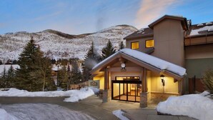 A hotel entrance with a snow-covered roof, a visible clock, and a mountain backdrop. - Aspen at Streamside at Vail (Vail)