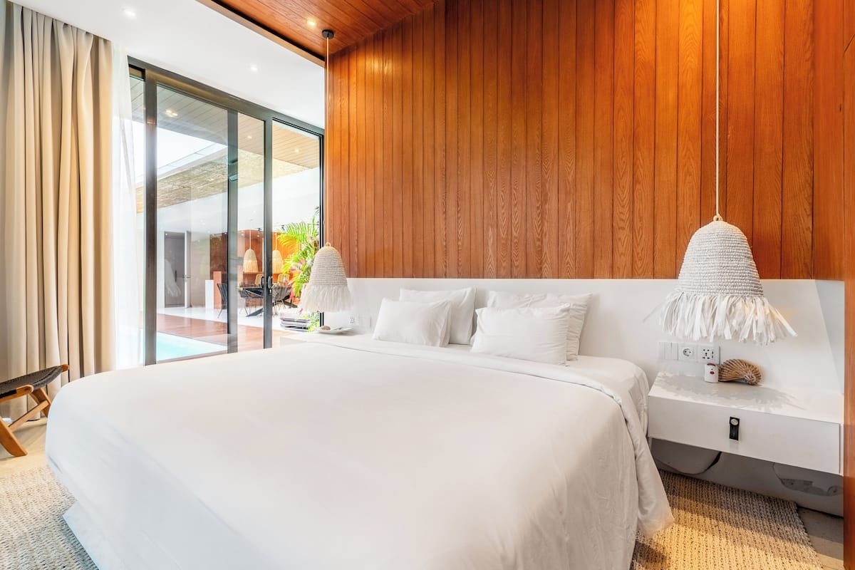 Un dormitorio moderno con una cama grande, paneles de madera y vista a un espacio exterior.