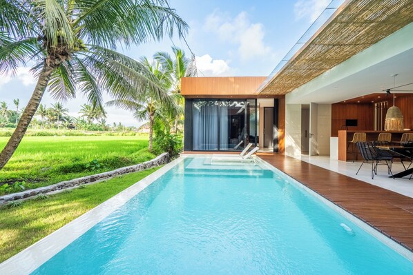 Un área de piscina moderna con vista despejada, terraza de madera y zona de comedor con sillas y mesa.