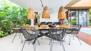A modern outdoor dining area with a glass table, black wicker chairs, and woven pendant lights. - Green Flow Villa 14 (Ubud)