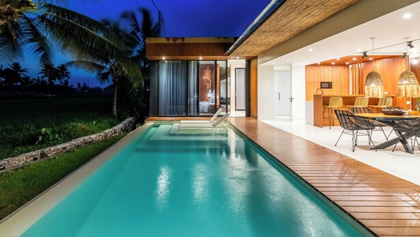 A modern poolside area with a wooden deck, a pool, and a dining area with chairs and a table. - Green Flow Villa 14 (Ubud)