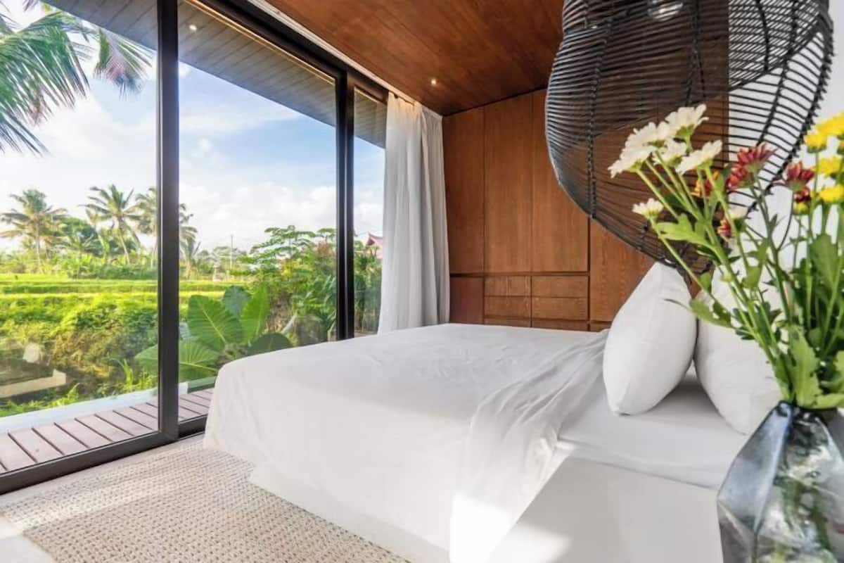 Un dormitorio con un ventanal grande, una cama con ropa de cama blanca y una silla colgante.