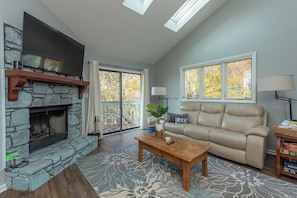 A living room with a stone fireplace, a leather sofa, a coffee table, and a TV mounted above the fireplace.