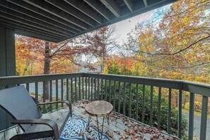 A covered outdoor deck with a metal railing, a wicker chair, a small round table, and a patterned rug.