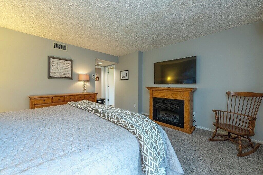 Une chambre à coucher avec un grand lit, une cheminée, une télévision et un fauteuil à bascule.