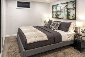 A bedroom with a bed, bedside lamps, a painting, and a carpeted floor. - Saddle Brook Studio with Patio - Near NYC! (Saddle Brook)