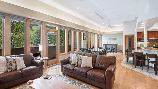 A spacious living room with leather sofas, a wooden coffee table, and large windows offering a view of the outdoors.