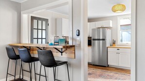 Una cocina moderna con un refrigerador de acero inoxidable, gabinetes blancos y una barra de madera con taburetes negros.