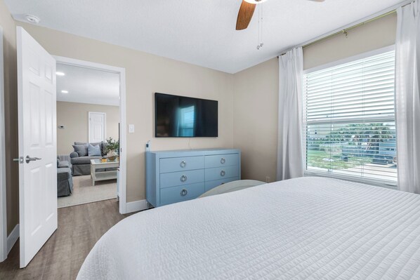A bedroom with a bed, a TV mounted on the wall, a dresser, and a window with blinds. - 🌊The Salt House | Bikes + Gear | Steps 2 Beach | Crow's Nest 🚲 (Pensacola Beach)
