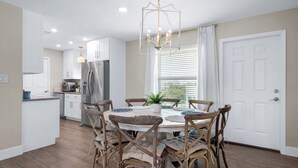 Una cocina moderna con armarios blancos, un refrigerador de acero inoxidable y un comedor con sillas de madera y una mesa redonda.