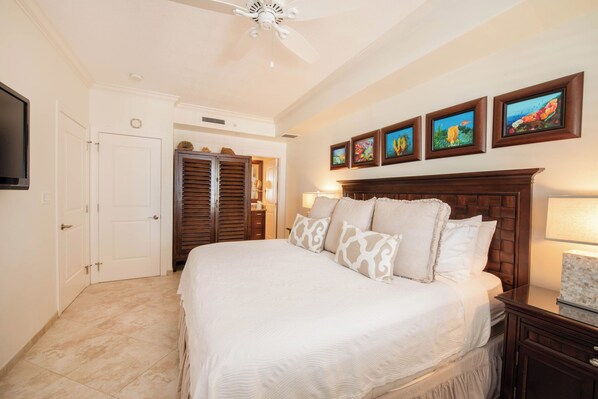 A bedroom with a large bed, a ceiling fan, a wardrobe, and framed artwork on the wall.