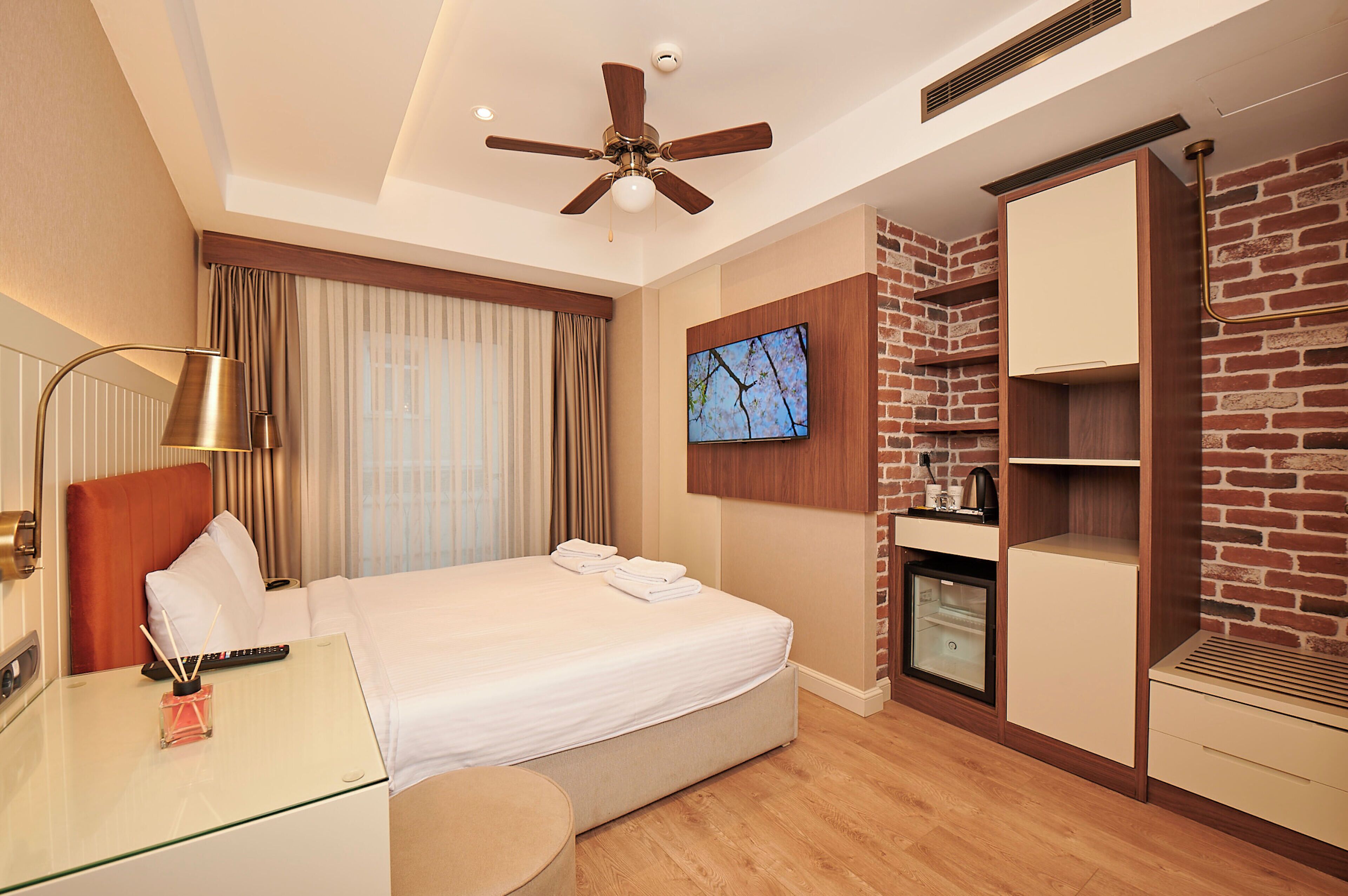 A hotel room with a bed, a desk, a television, a wardrobe, and a ceiling fan.
