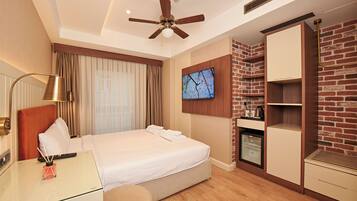 A hotel room with a bed, a desk, a television, a wardrobe, and a ceiling fan.