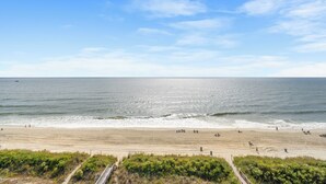 A beach with a clear sky, sandy shore, and a few people walking. - Recently Renovated Oceanfront Condo + Free Attraction Tickets! (North Myrtle Beach)