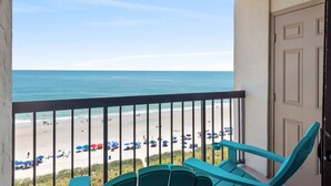 A balcony with a view of a beach, featuring a door and a chair. - Recently Renovated Oceanfront Condo + Free Attraction Tickets! (North Myrtle Beach)