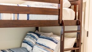 A bunk bed with a striped bedspread and pillows, wooden headboard, and a carpeted floor.