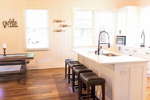 A kitchen with wooden flooring, a bar stool, a sink, and a window with blinds. - Chalet Premiere at Signal Point (Guntersville)