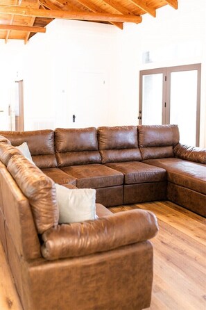 A brown leather sectional sofa with a light-colored pillow in a room with wooden flooring and a wooden ceiling. - Chalet Premiere at Signal Point (Guntersville)