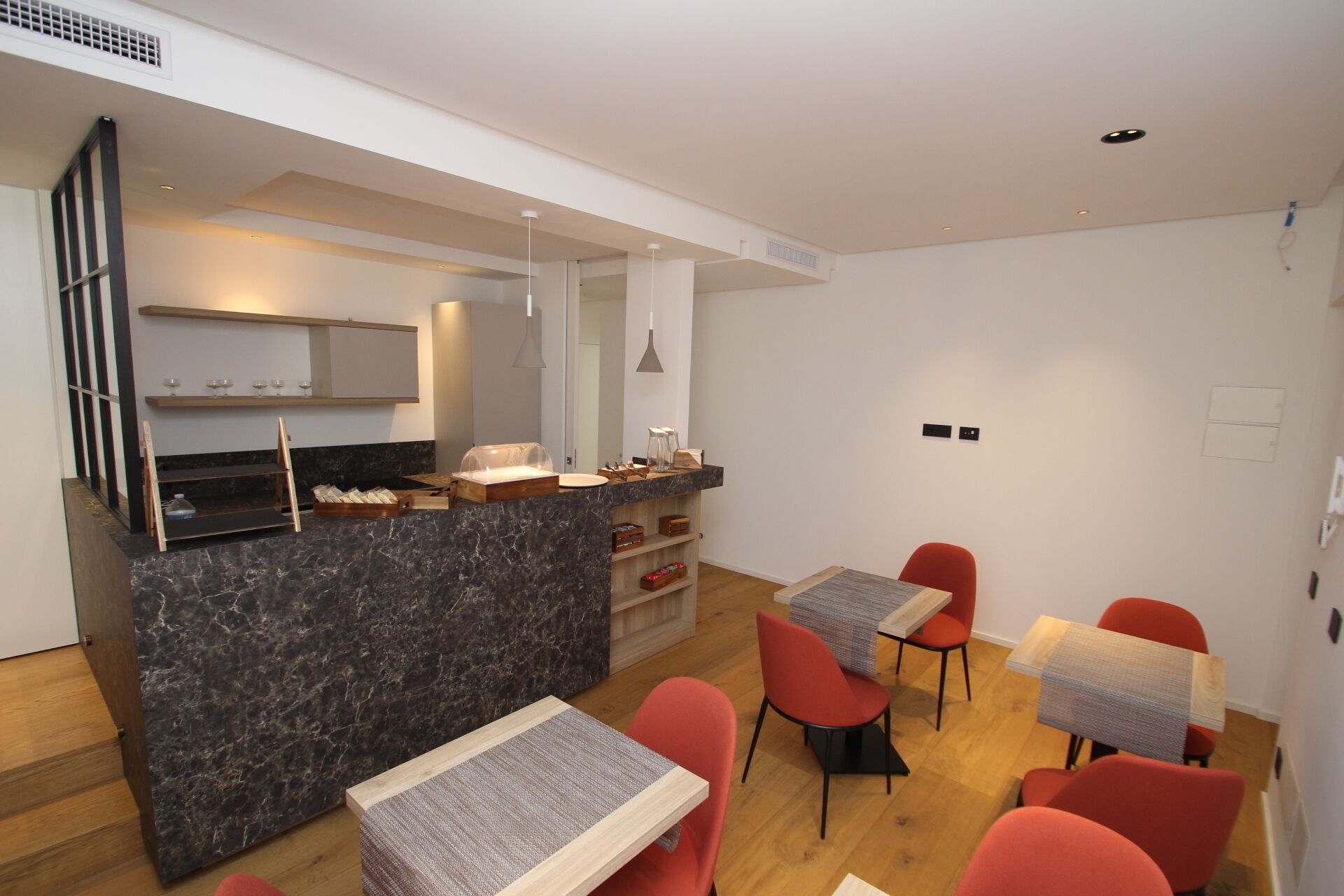 A modern kitchen with a marble countertop, wooden cabinets, and a built-in oven. There are two red chairs and a small table with a woven table runner.