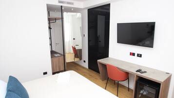 A modern hotel room with a bed, a desk, a chair, a television, and a wardrobe.