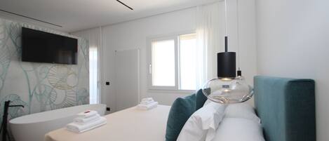Una habitación de hotel moderna con una cama, un ventanal amplio, un televisor y un baño con bañera.