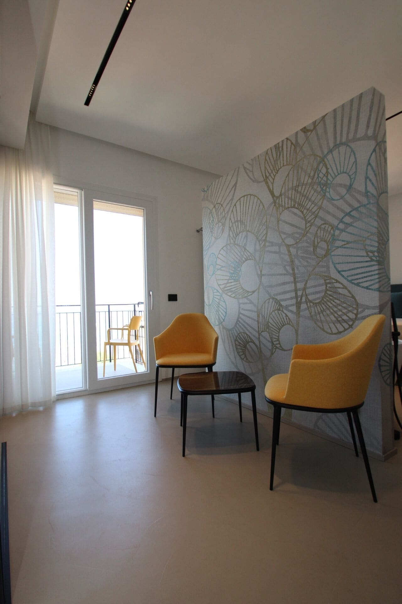 A modern living room with two yellow chairs, a small table, and a large abstract wall mural.