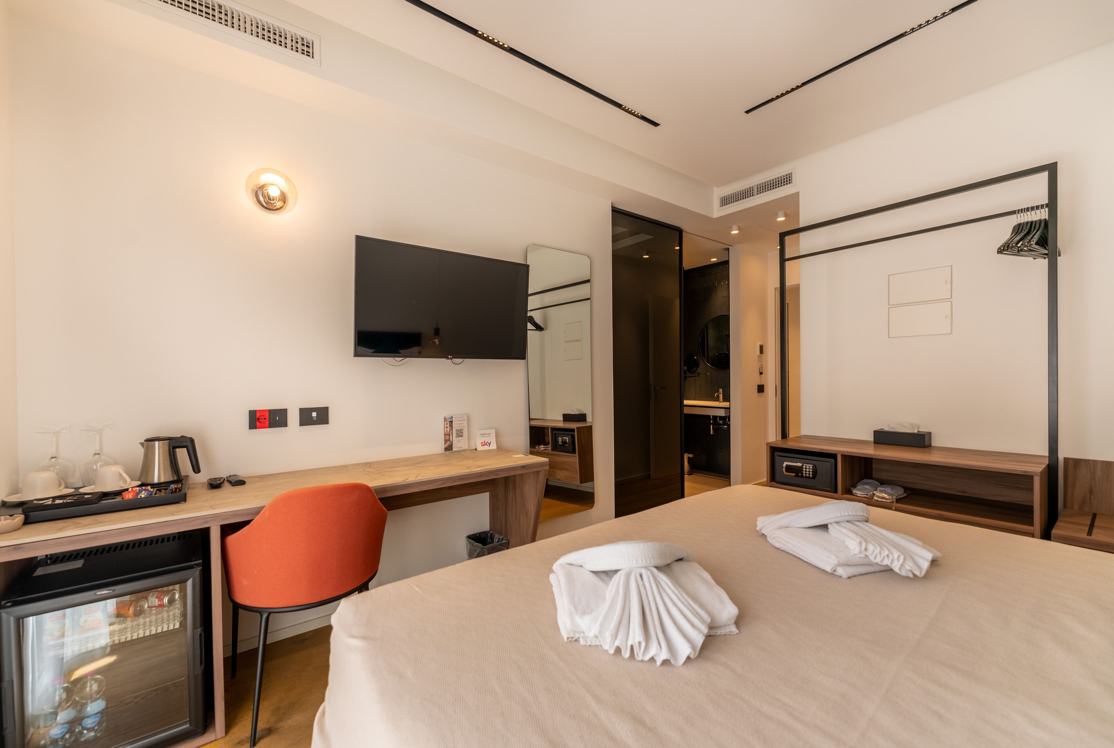 Een hotelkamer met een bed, een bureau met computer, een stoel, een aan de muur bevestigde televisie, een minibar en een kledingkast.