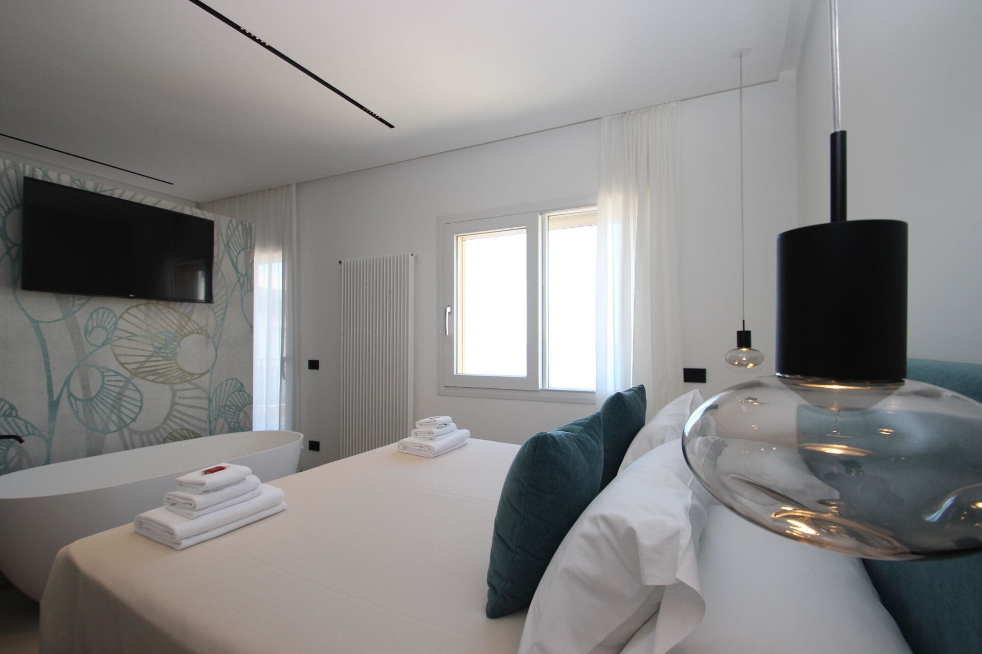 Una habitación de hotel moderna con una cama, un espejo grande, un televisor de pantalla plana, una ventana con cortinas y un radiador.