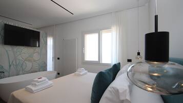 Ein modernes Hotelzimmer mit Bett, großem Spiegel, Flachbildfernseher, Fenster mit Vorhängen und Heizkörper.