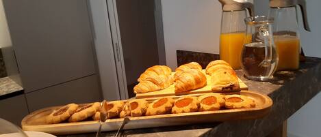 Un bufé de desayuno con cruasanes, pastelería y una jarra de jugo sobre una encimera de mármol.
