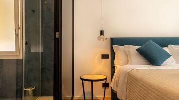 Habitación de hotel con cama, una mesita, luz en la pared y zona de ducha.