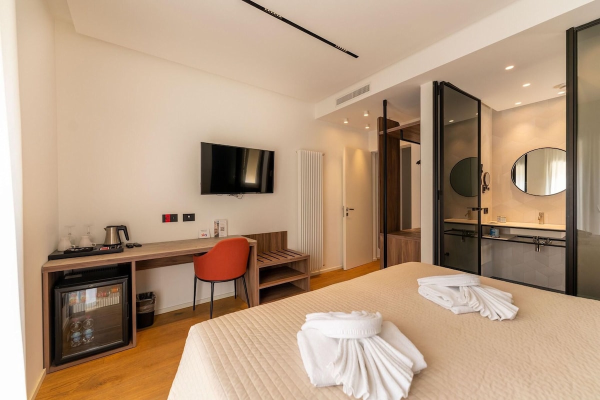 Une chambre d’hôtel comprenant un lit, un bureau avec une chaise, une télévision, un minibar et une salle de bain avec un miroir et un lavabo.