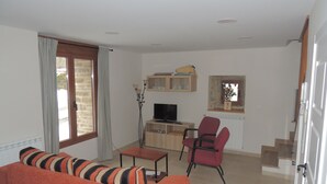 Ein Wohnzimmer mit einer Couch, einem Fernseher, einem Esstisch und einem Stuhl.