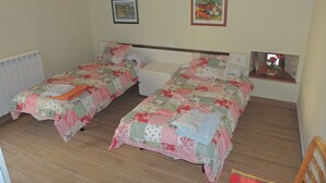 Ein Schlafzimmer mit zwei Einzelbetten, Holzbalkendecke, einem kleinen Nachttisch mit Lampe und einem gerahmten Bild an der Wand.