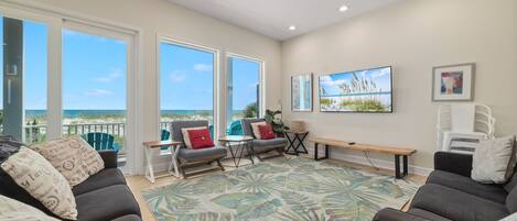 A spacious living area with a large window overlooking the beach, a comfortable seating arrangement, and a tropical-themed rug.