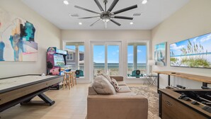 A spacious living room with a pool table, a sofa, and a large TV screen.