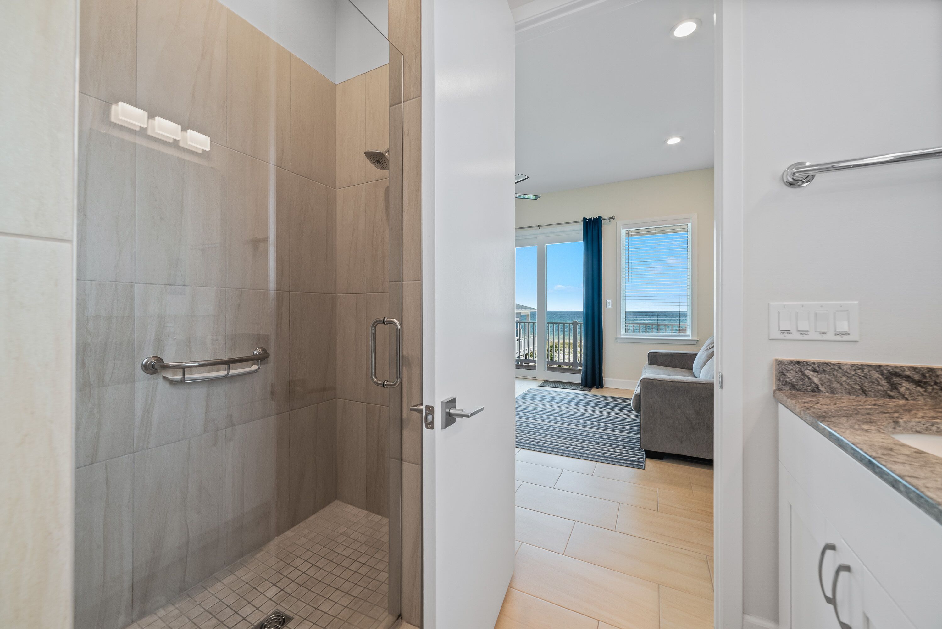 Un baño moderno con ducha, barras de apoyo y vistas al salón.