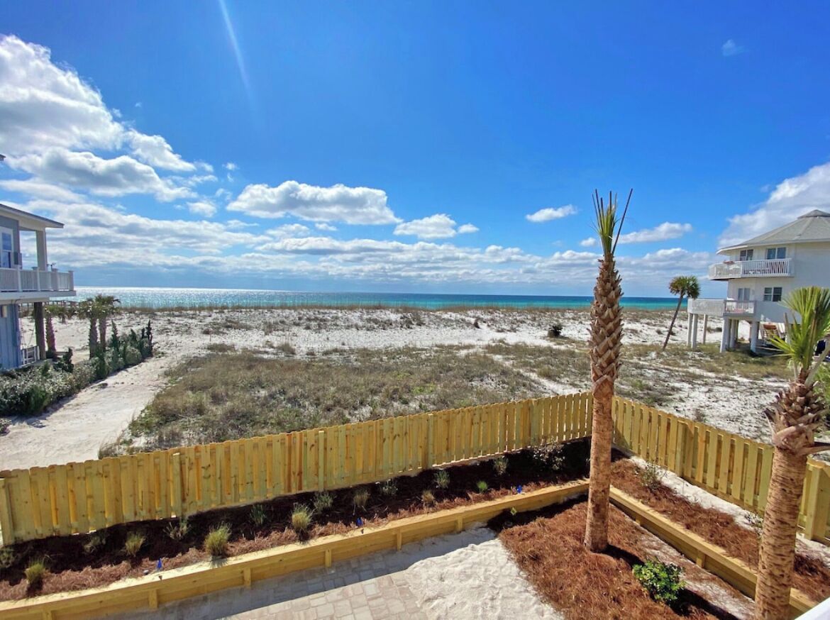 A beachfront property with a wooden fence, a palm tree, and a view of the ocean.