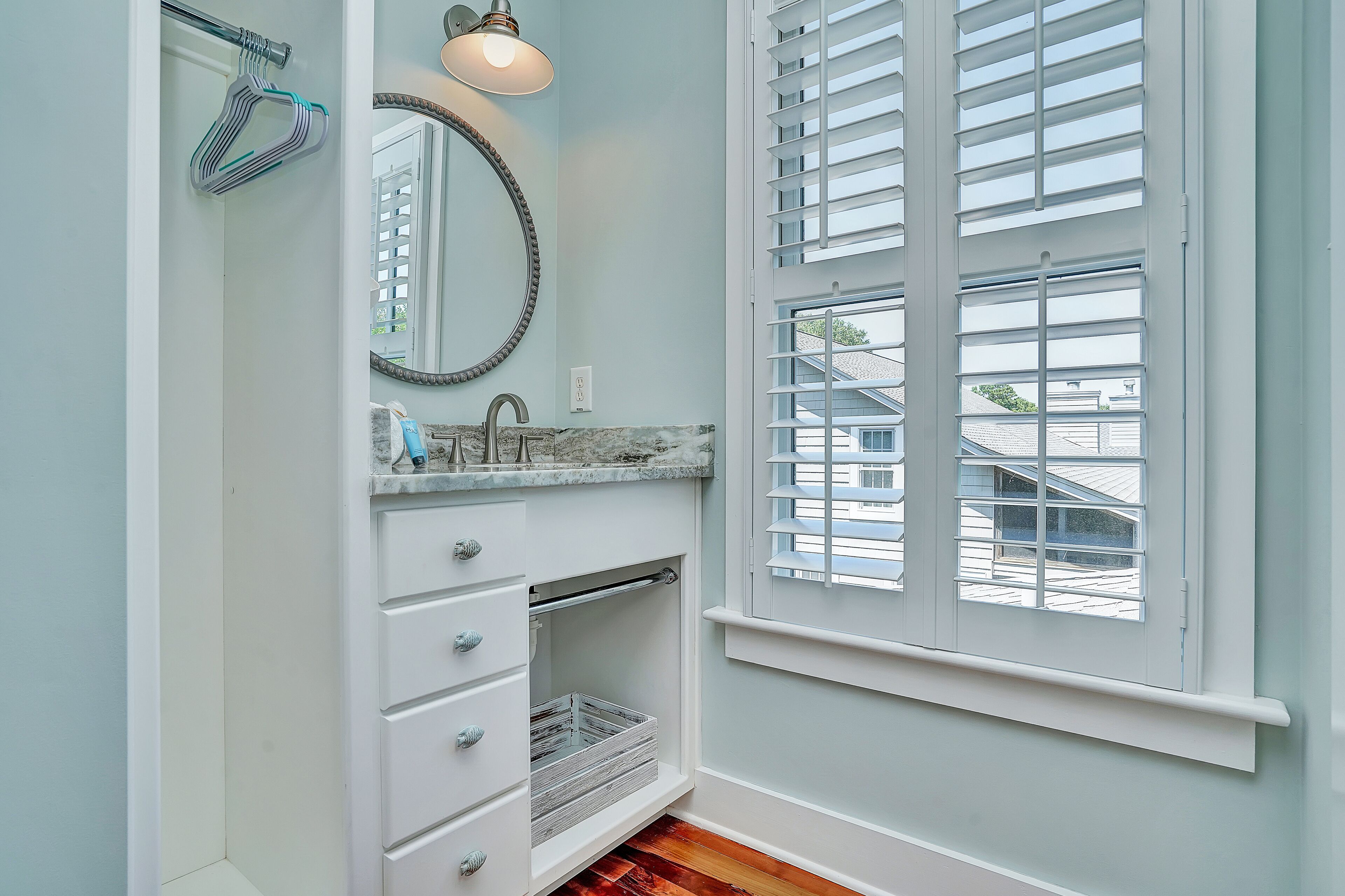 A bathroom with a white vanity, a mirror, a sink, and a window with shutters.