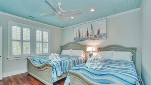 Un dormitorio con dos camas, un ventilador de techo y una pintura de veleros.
