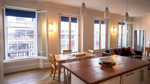 A modern kitchen with a wooden island, dining table, and chairs. There are pendant lights, a view of the outside, and a large window with a view of the city. - Central 1-bed Apartment in Inverness, Sleeps 4 (Inverness)