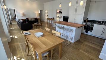 A modern kitchen with white cabinets, a wooden dining table, and bar stools.