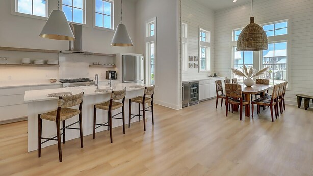 A modern kitchen with a central island, bar stools, and a dining table with chairs.